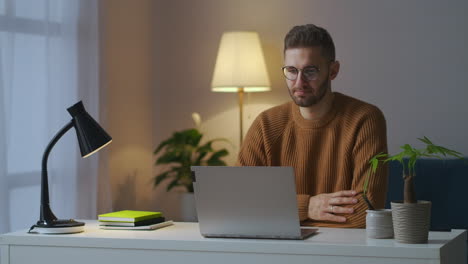 portrait-of-male-participant-of-working-video-chat-man-is-nodding-his-head-viewing-display-of-laptop-sitting-in-home-at-evening-remote-communication